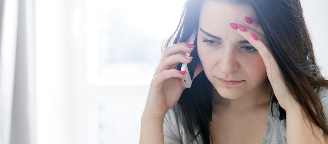 Unhappy worried young woman talking on phone at home