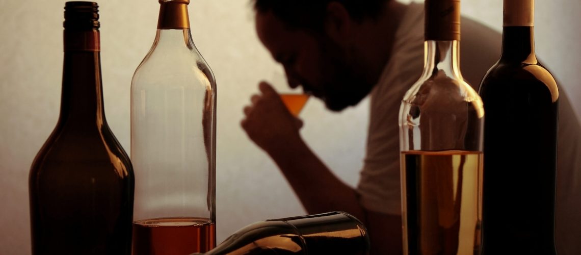 silhouette of anonymous alcoholic person drinking behind bottles of alcohol