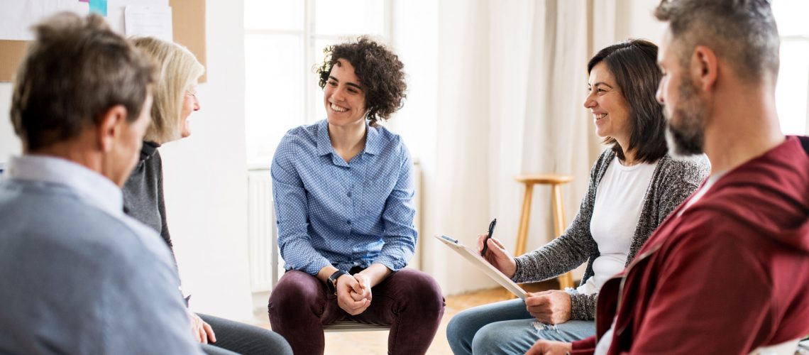 Serious men and women sitting in a circle during group therapy, talking.