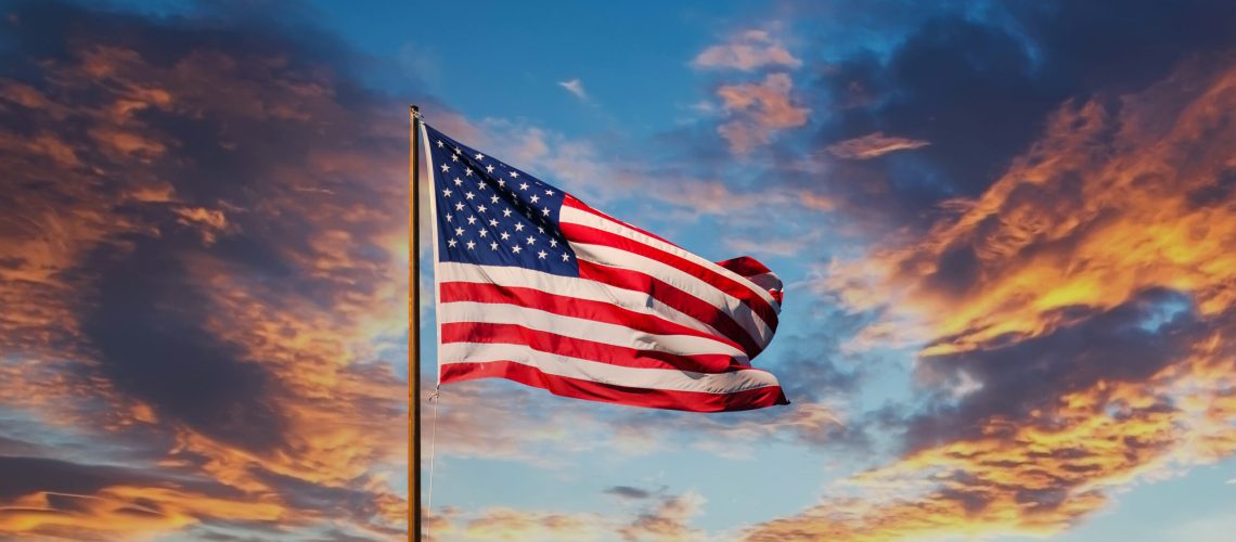 An American flag against a blue sky on an old rusty flagpole
